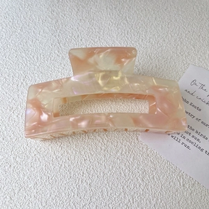 Detail view of a large square acetate hair claw clip with pink marble texture on paper