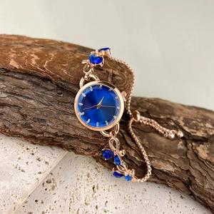 Detail of rose gold bracelet watch with dark blue dial on rustic wood and stone blocks