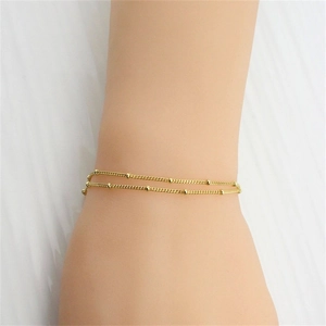Detail of minimalist gold double-layered beaded chain bracelet on model's wrist