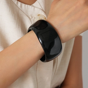 Close-up of a wide black acrylic bangle with a high-gloss finish on a model wrist