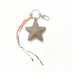 Detail of star-shaped leather keychain with grey-brown finish and printed fabric tassel