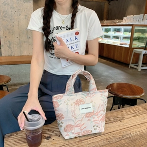 Florale geprägte Lunchtasche mit Reißverschluss auf einem hölzernen Cafétisch