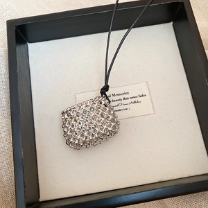 Detail of silver woven hollow pendant on a black cord placed in a luxury display box