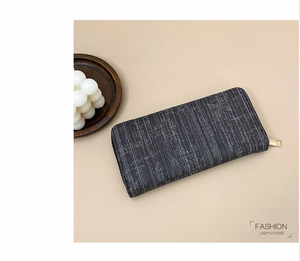 Detail view of a long dark grey striped wallet for women with golden zipper on a tray