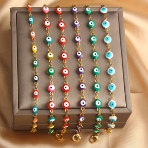 Detail view of colorful evil eye bracelets with gold chains and enamel charms on silk