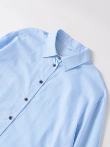 Detalle del cuello de una camisa azul claro con botones a juego y textura de algodón suave