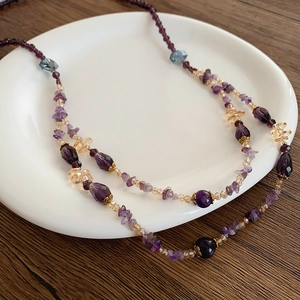 Detail einer mehrschichtigen Amethyst-Halskette in weißer Keramikschale auf Holzhintergrund