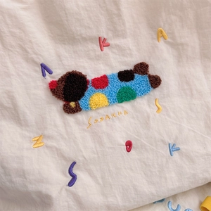 Detail of towel embroidery dachshund pattern on cream canvas tote bag with letter accents