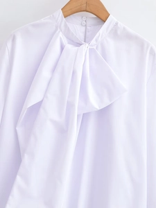 Close-up of white blouse with elegant bow tie, stand collar and two delicate buttons