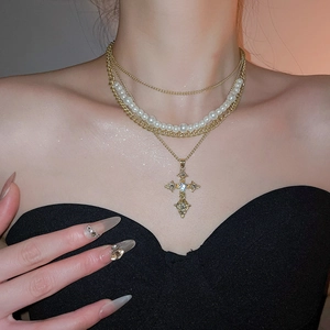 Detail of layered gold necklace with white pearls and sparkling rhinestone cross pendant