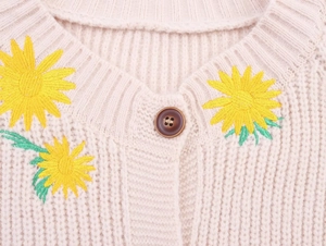 Close-up of cream knit cardigan featuring detailed sunflower embroidery and brown button