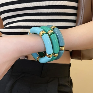 Detail of colorful acrylic tube bracelets in blue and green with gold metal accents