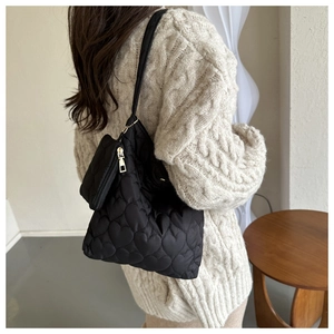 Detail of black heart-quilted tote bag with matching coin purse shown on a model