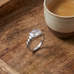 Detail of twisted texture silver ring with a rectangular clear stone on wooden tray
