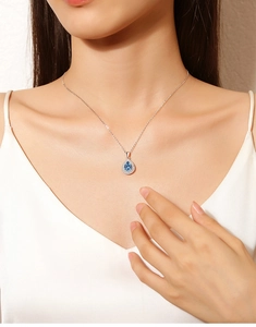 Close-up of teardrop blue gemstone pendant necklace worn by a model with silver chain