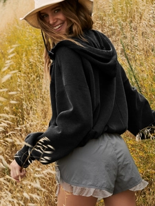 Outdoor shot of a women's black zip-up hoodie paired with grey shorts and a beige bucket hat