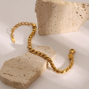 Macro detail of chunky gold-plated braided chain bracelet on textured mineral stones