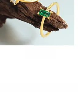 Makro-Detail eines vergoldeten Rings mit grünem Edelstein auf einem Ast aus Holz