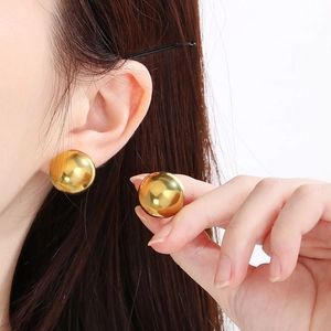 Close-up of a model wearing high-polished gold spherical stud earrings with glossy finish