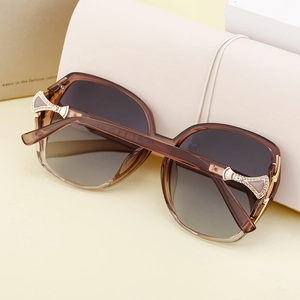 Détail de lunettes de soleil carrées ambre avec branches dorées ornées de strass