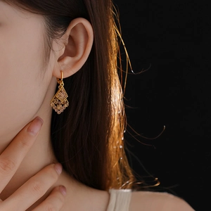 Detail of model wearing gold diamond rhombus leaf earrings with champagne stones