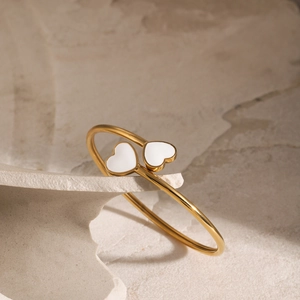 Close-up of 18k gold plated bangle with two white enamel hearts on stone display