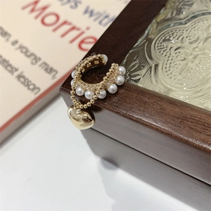 Dettaglio ear cuff a C dorato con perle e ciondolo a cuore su scatola di legno scuro