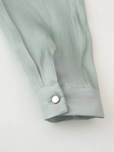 Detailed close-up of light green satin shirt cuff with a polished silver button fastener