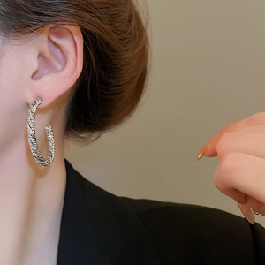 Close-up of a silver twisted C-shaped hoop earring worn by a model in a black blazer