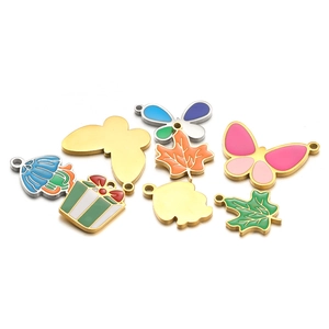 Detailed flat lay of colorful enamel butterfly and maple leaf pendants with gold-plated edges