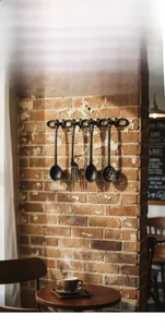 Dettaglio di ganci da cucina vintage in ghisa con mestolo e forchetta su muro di mattoni