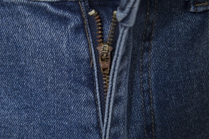 Macro detail of dark blue denim jeans showing a brass zipper and reinforced stitching