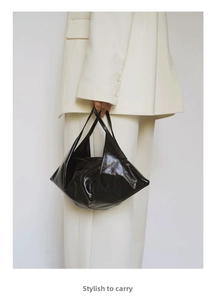 Close-up of black glossy leather handbag with soft geometric design and twin handles