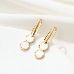 Detail of elegant gold-tone pearl hoop earrings featuring white shell inlay on white fabric