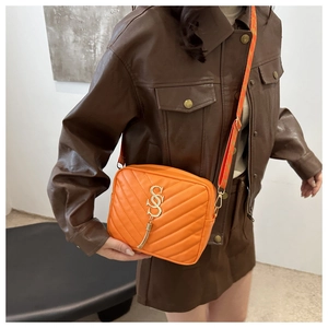 Detail of orange quilted crossbody bag with golden hardware and patterned shoulder strap