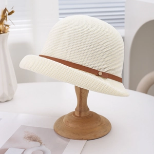 Detail of a beige woven sun hat featuring a brown leather strap and gold rivet on wood stand