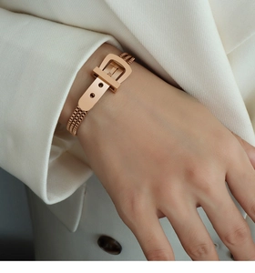 Detailed view of rose gold belt buckle bracelet worn over an elegant beige suit