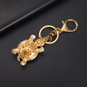Detail of a golden turtle keychain with hollow shell design on black leather surface