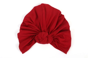 Detailed view of red knitted turban hat featuring central knot and pleated texture