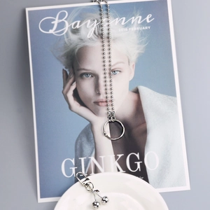 Silver bead chain necklace with circular pendant and cherry charm on a magazine