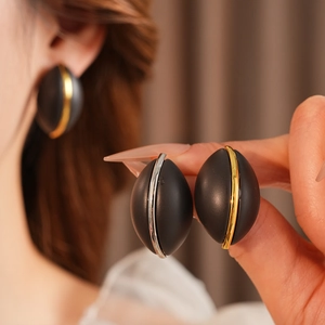 Dettaglio di orecchini ovali nero opaco con strisce metalliche in oro e argento