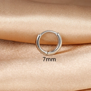 Detail showing 7mm diameter minimalist huggie earrings on champagne satin background
