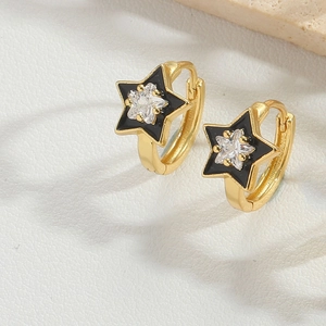 Detailed close-up of gold star earrings with black enamel and zircon on white leather