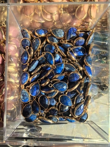Bulk display of teardrop dark blue lapis stone pendants with gold metal edge in a clear box