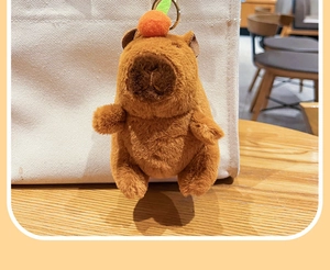 Plush brown capybara keychain with orange decoration on a white canvas bag detail