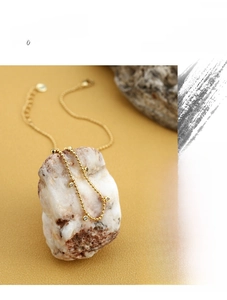 Close-up of gold beaded necklace featuring sparkling zircon charms on a textured stone base