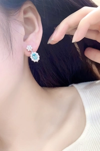 Macro shot of a floral silver earring with light blue oval gemstone on a model