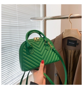 Detail of green shell-shaped bag with V-quilted pattern and golden hardware held by model