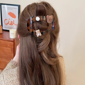 Detail view of a tortoise shell hair claw with plush bears and pearls on long wavy hair