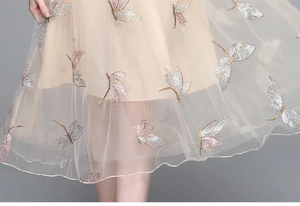 Detail of dragonfly and butterfly embroidery on champagne sheer mesh fabric